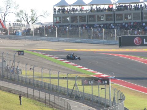 2006 BMW 5 Series - A single-seat race car navigates a turn on a professional racetrack with spectators in the background.