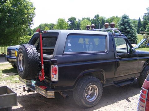 1996 Ford Bronco - Rear view of a black Ford Bronco, showing its spare tire carrier and a second vehicle behind it.