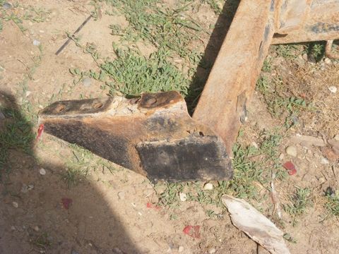 1996 Ford Bronco - Close-up of a heavily rusted metal bracket, possibly a vehicle part, lying on the ground.