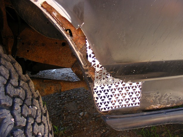 Close-up of a heavily rusted wheel well with a metal patch, showing a tire and part of the vehicle body