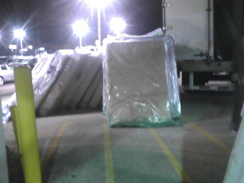 2003 Ford Crown Victoria - Mattresses are stacked and wrapped in plastic, illuminated by bright lights in a parking lot.