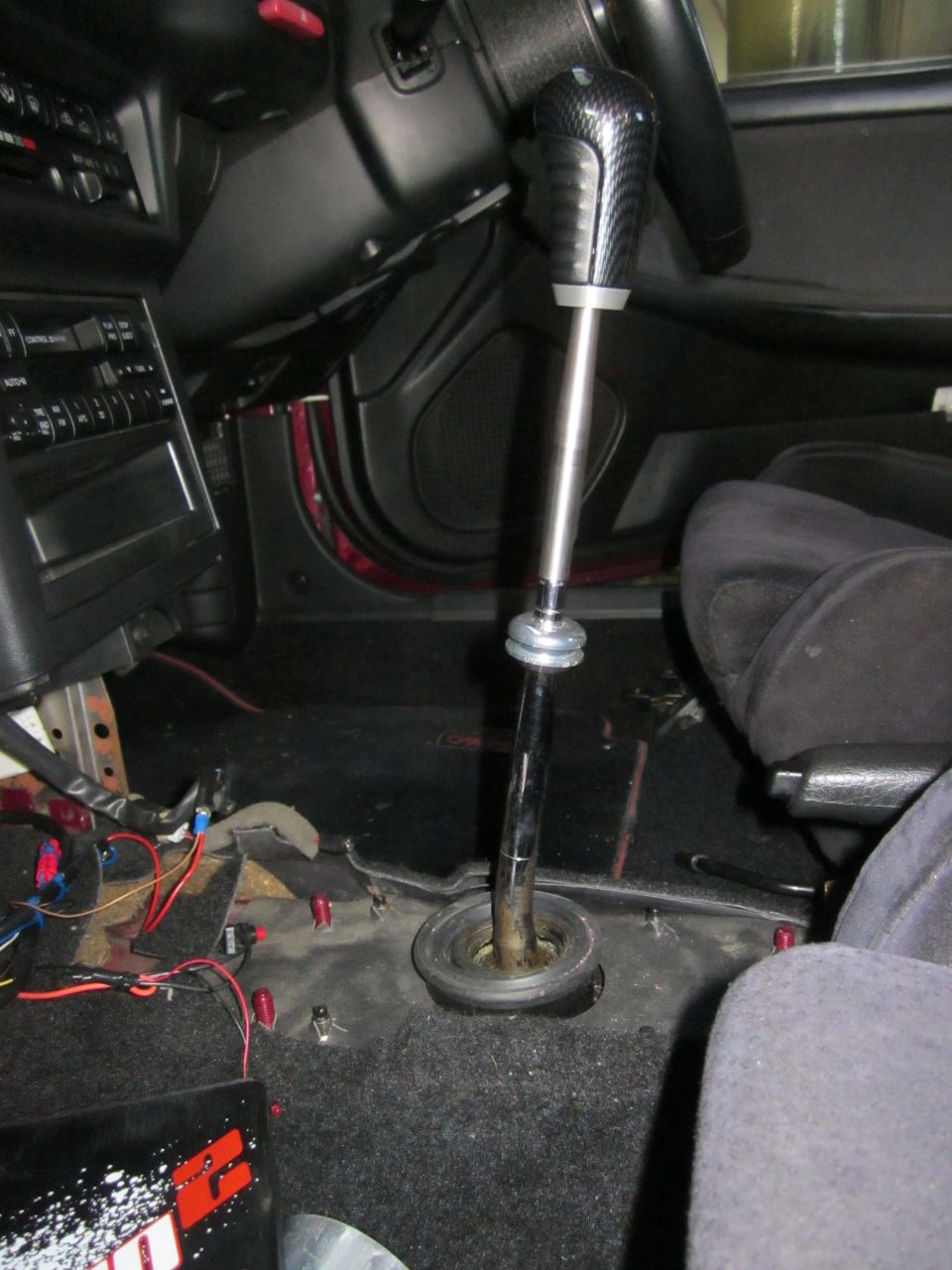 Car interior showing a custom short shifter with a carbon fiber knob. The center console is partially disassembled