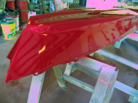 1970 Ford Mustang - A freshly painted red car hood rests on sawhorses, with the Supermotors.net logo in the lower right corner.