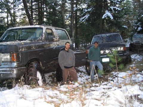 1988 Ford Bronco - Two muddy SUVs, including a 1988 Ford Bronco, sit in a snowy, wooded area after off-roading.