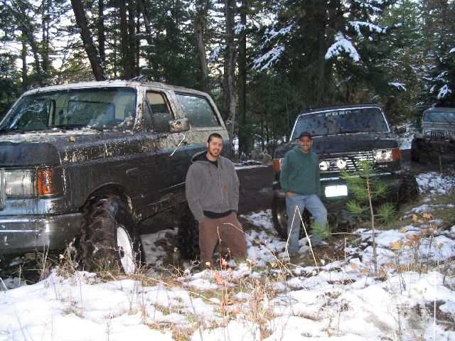 1988 Ford Bronco and another SUV covered in mud, parked in a snowy forest