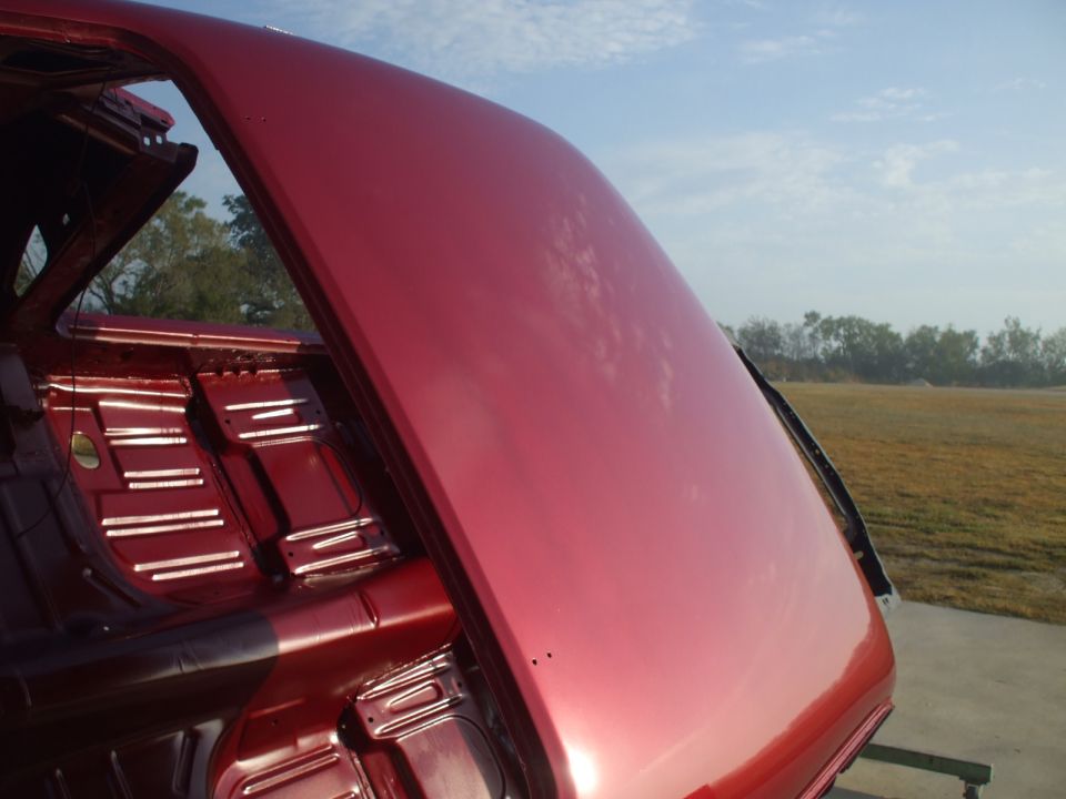 Red car interior showing bare metal floor and rear seat area, with the trunk lid open