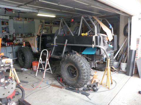 1961 International Scout 800 - A custom off-road vehicle is in a garage, undergoing construction with a prominent roll cage and large tires.
