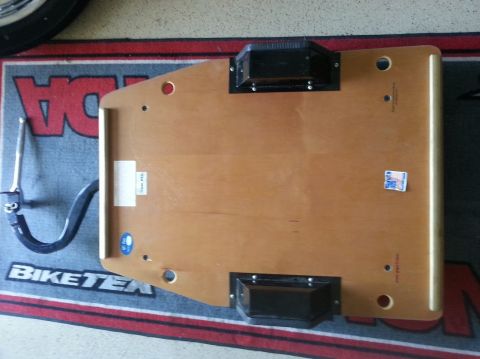 1978 Ford Bronco - A wooden dolly with black rollers is shown on a mat, with visible text on the mat and a sticker on the dolly.