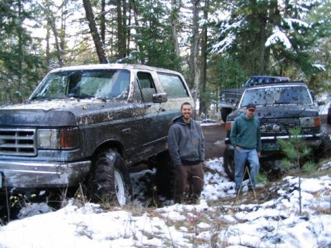 1988 Ford Bronco - Two men stand next to a very muddy Ford Bronco and another off-road vehicle in a snowy, wooded environment.