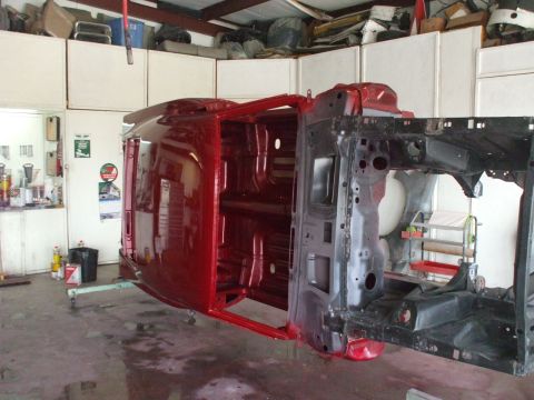 1970 Ford Mustang - The underside of a car body is painted red while it's mounted on a rotisserie for restoration.