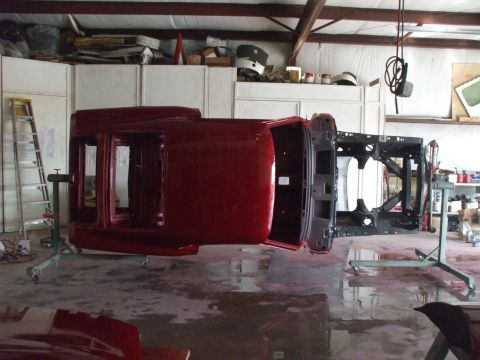 1970 Ford Mustang - A red 1970 Ford Mustang body is shown upside down on a rotisserie, likely undergoing restoration or painting.