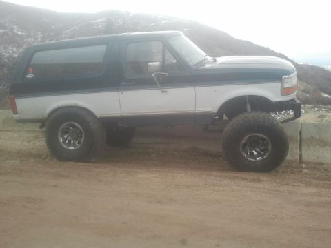 1994 Ford Bronco - Side view of a lifted 1994 Ford Bronco with two-tone paint and large off-road tires.