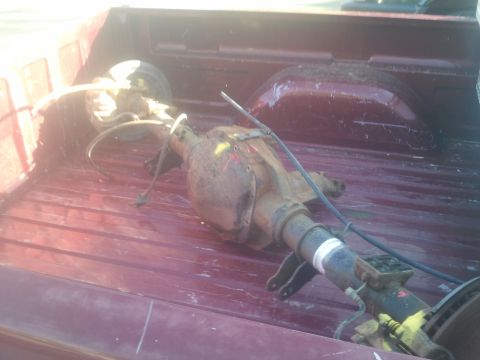 1994 Ford Bronco - A rusty rear axle assembly is loaded into the bed of a red pickup truck.