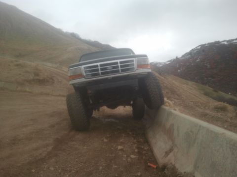 1994 Ford Bronco - A black Ford Bronco is shown from the front, with its tires on a concrete barrier on a dirt hill.