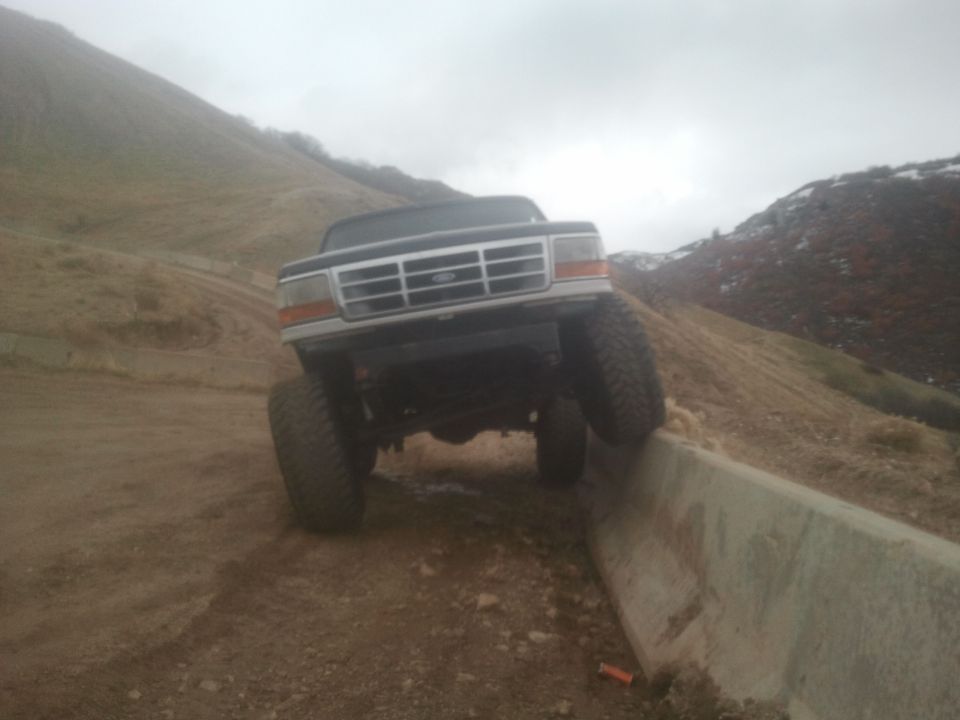 Black Ford Bronco with large tires on a dirt incline, front view