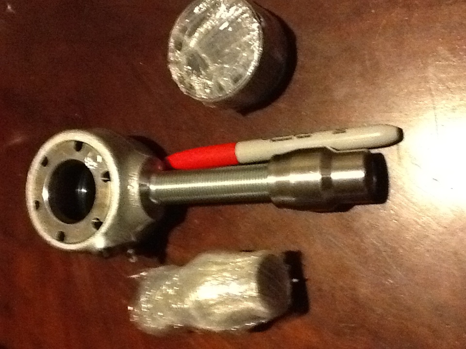 Metal automotive part with threaded rod, a red-tipped marker, and two wrapped components on a wooden surface