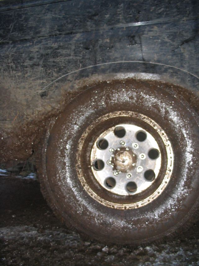 Mud-covered tire and wheel on a dark vehicle
