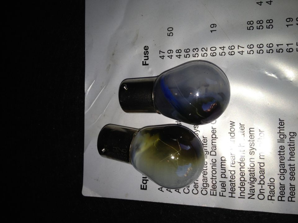 Two automotive light bulbs resting on a fuse chart with various electrical components listed