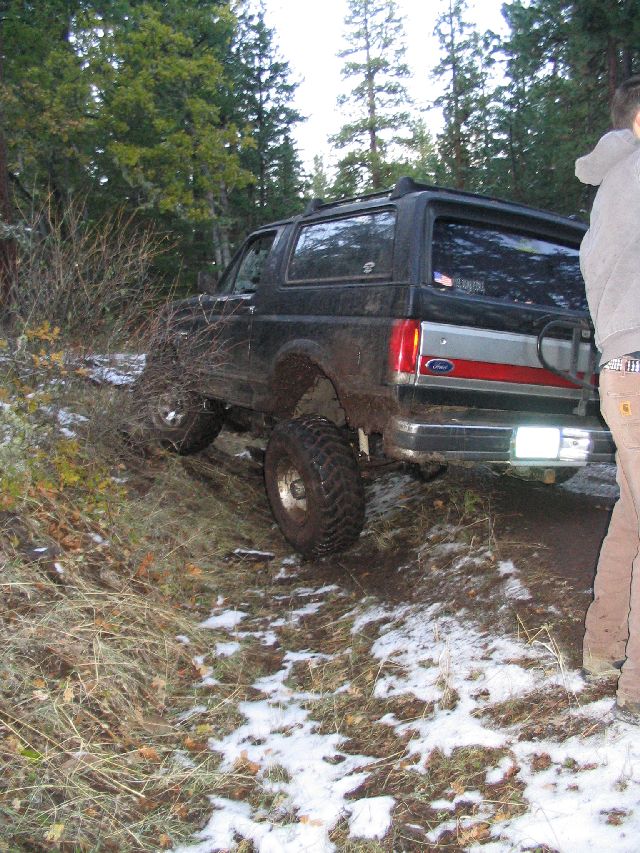 1988 Ford Bronco on a dirt trail with snow patches, trees in background