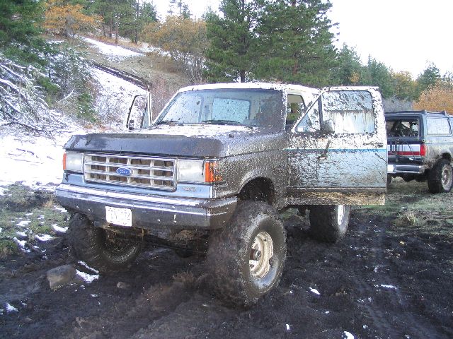Muddy Ford Bronco with doors open, another Bronco behind it, in a snowy, muddy area