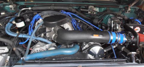 1990 Ford Bronco - Engine compartment showing a black K&N intake tube, blue spark plug wires and an alternator on a green-painted vehicle.