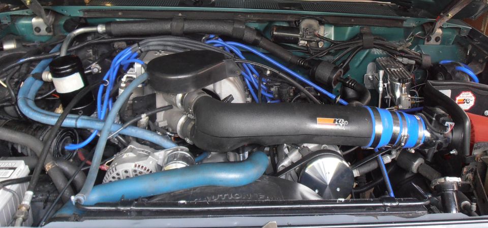 Engine bay with K&N intake tube and blue spark plug wires on a green vehicle