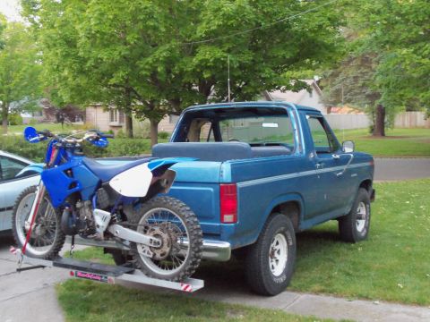 1985 Ford Bronco - A blue 1985 Ford Bronco is shown with a dirt bike mounted on a carrier attached to the trailer hitch.