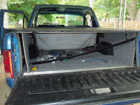 1985 Ford Bronco - The bed of a 1985 Ford Bronco is carpeted and contains tools and a spare tire.