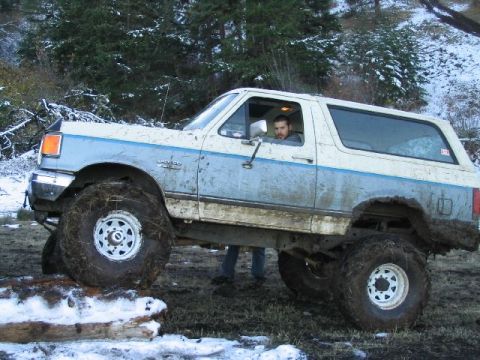 1988 Ford Bronco - This lifted Ford Bronco is navigating rough terrain with large off-road tires.