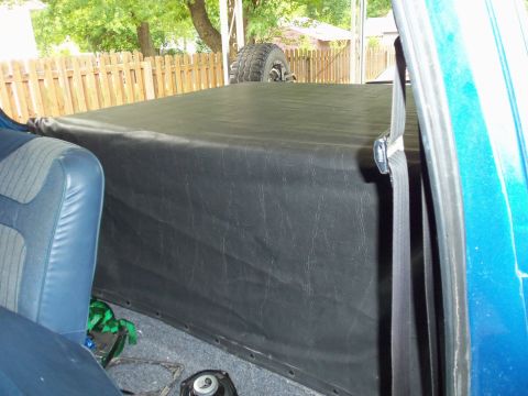 1985 Ford Bronco - The cargo area of the vehicle is covered with a black vinyl tarp, with a spare tire visible on top.