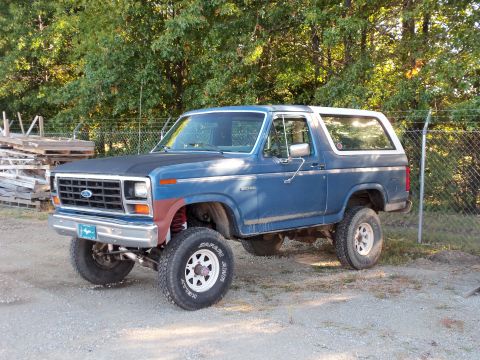 1985 Ford Bronco - This blue Ford Bronco has a modified suspension and sits on white spoke wheels.