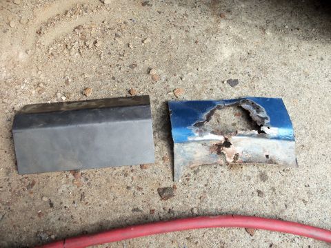 1985 Ford Bronco - Two automotive parts, one a heavily rusted blue panel and the other a grey trim piece, lie on a gravelly surface.
