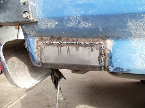 1985 Ford Bronco - Welding repair on the lower body panel of a blue vehicle.