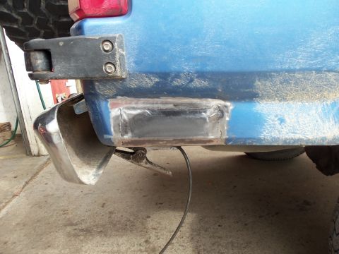 1985 Ford Bronco - Close-up of a blue vehicle's rear quarter panel showing bodywork and a chrome bumper attachment.