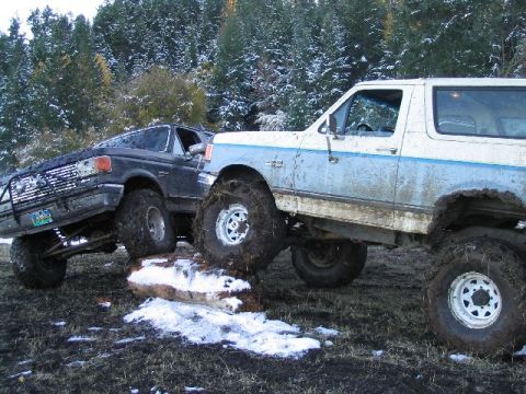 1988 Ford Bronco - Two SUVs tackle a challenging course in a snowy, wooded area.