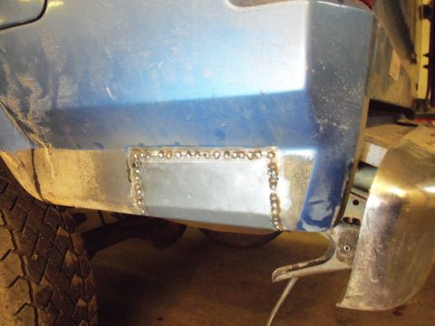 1985 Ford Bronco - Welded patch repair on the rear quarter panel of a blue vehicle, with a Supermotors.net logo in the corner.