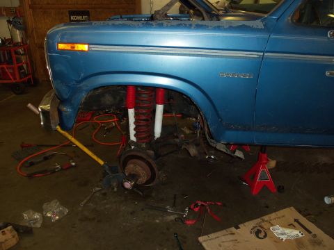1985 Ford Bronco - A blue Ford Bronco is shown in a garage with its front suspension disassembled and lifted on jack stands.