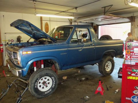 1985 Ford Bronco - 1985 Ford Bronco undergoing work in a garage with its hood raised.