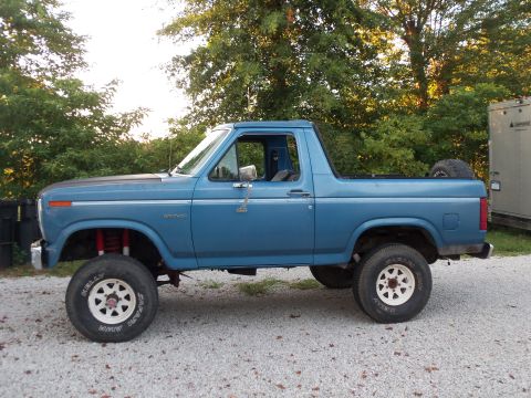 1985 Ford Bronco - Side view of a blue Ford Bronco with a lifted suspension and off-road tires parked outdoors.