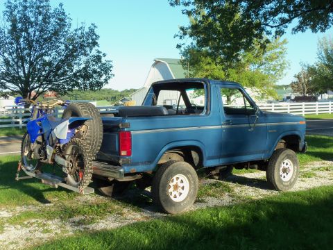1985 Ford Bronco - Blue Ford Bronco parked outdoors with a dirt bike on a rear rack.
