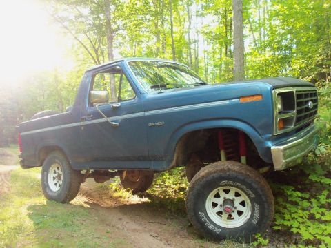 1985 Ford Bronco - This lifted 1985 Ford Bronco is shown off-road in a wooded setting.
