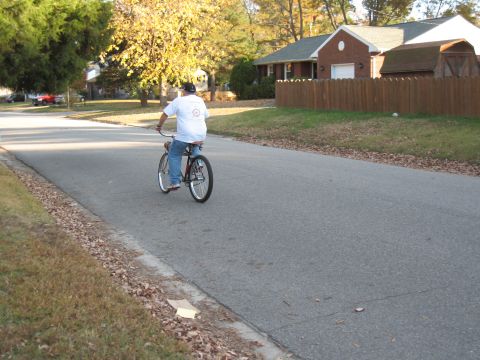 1994 Ford Bronco - A person rides a bicycle on a paved road in a residential area, with houses and trees in the background.