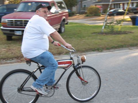 1994 Ford Bronco - Man rides a vintage bicycle past a red Ford Bronco on a suburban street.