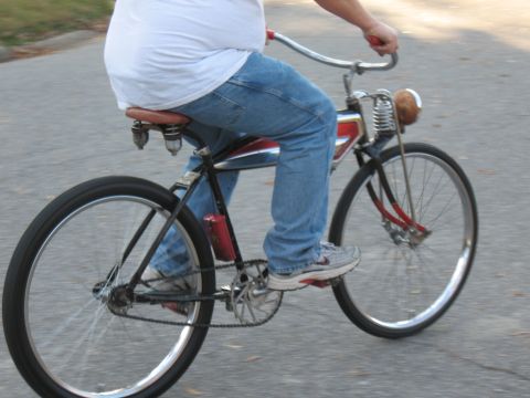1994 Ford Bronco - A person rides a classic bicycle with a leather seat and chrome handlebars down a paved road.