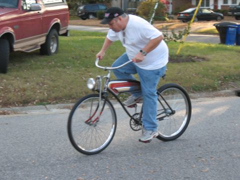 1994 Ford Bronco - A man rides a custom bicycle down a residential street, with a red pickup truck parked nearby.