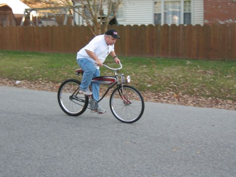 1994 Ford Bronco - Man rides a vintage bicycle down a suburban street past a wooden fence and houses.