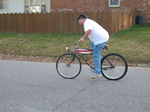 1994 Ford Bronco - A man rides a classic bicycle with a red stripe on the frame past a wooden fence and houses.