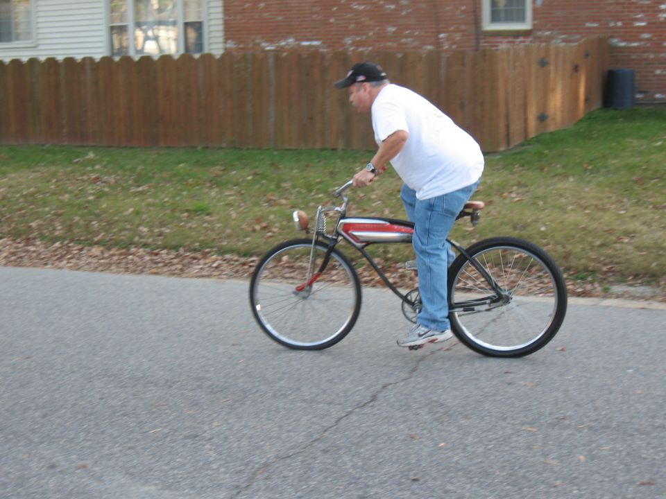 Man in white t-shirt and jeans riding a black and red vintage bicycle down a street