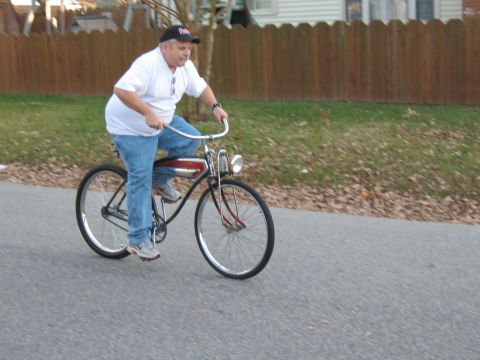 1994 Ford Bronco - A man rides a classic bicycle down a paved road with a wooden fence and houses in the background.