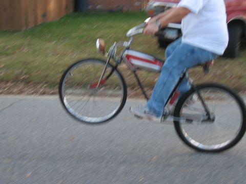 1994 Ford Bronco - A person rides a vintage-style bicycle with a red and white frame, performing a wheelie on a paved road.